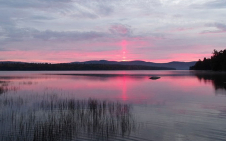The sky appears in shades of purple and pink, and is reflected on a lake. 
